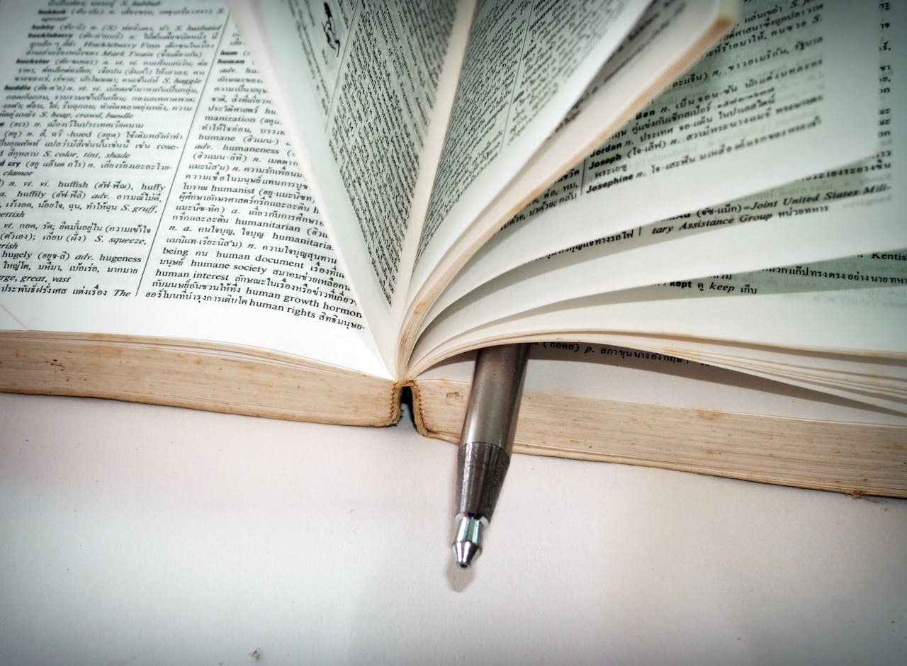 A close-up of an open dictionary with a pen separating the pages for convenient reference.