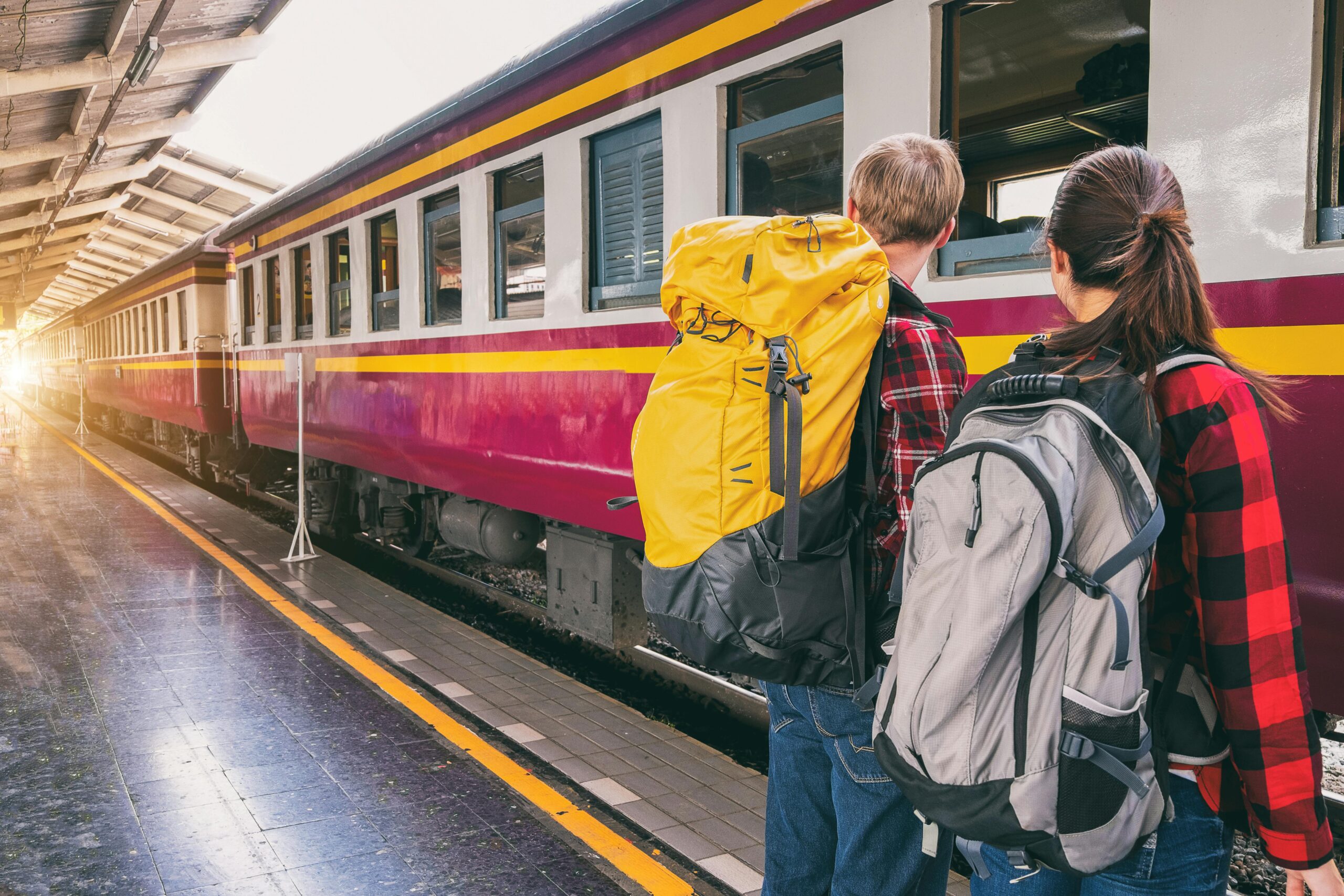 Backpackers waiting at a train station platform, ready for travel adventure.