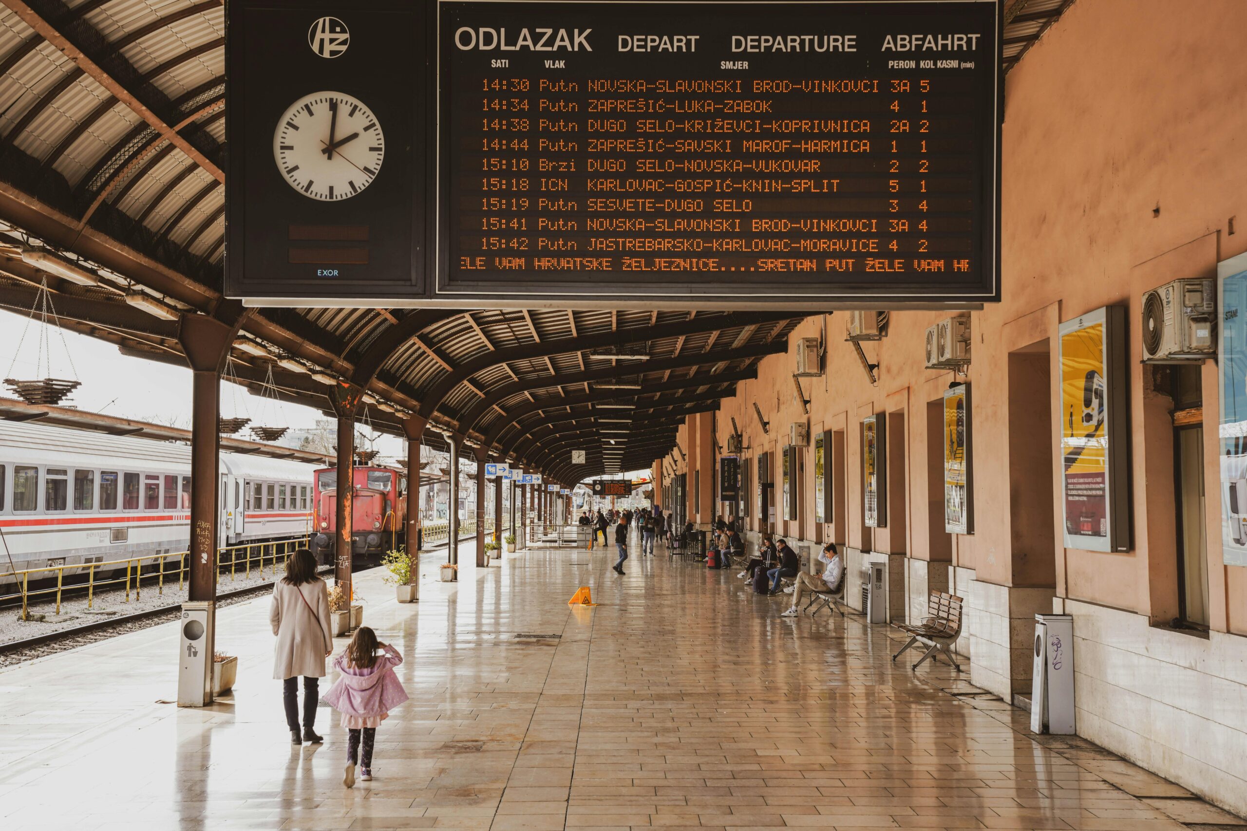 Busy train station in Zagreb with passengers and a large timetable display.