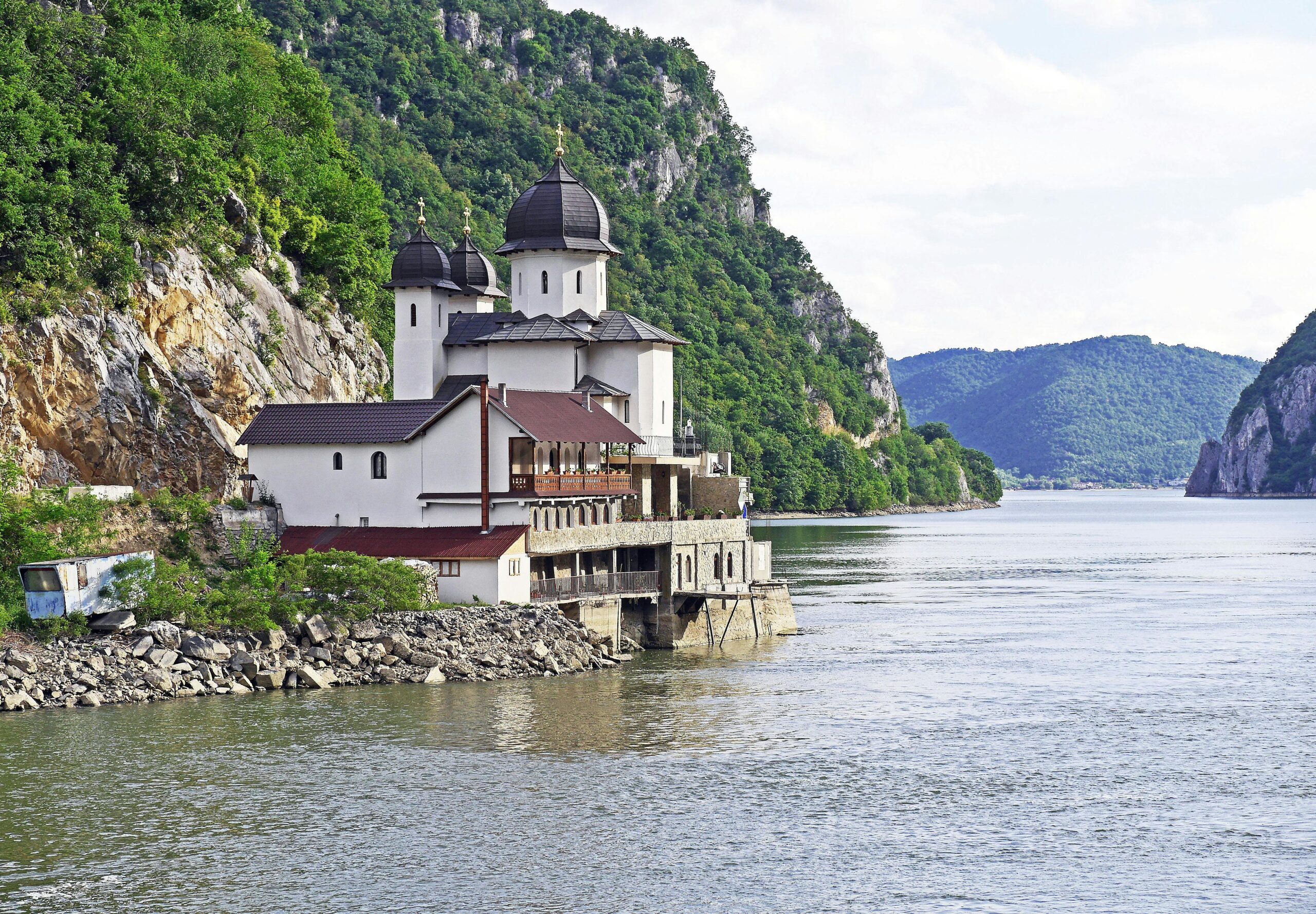 Scenic Orthodox monastery by the Danube River gorge in summer, set against lush green mountains.