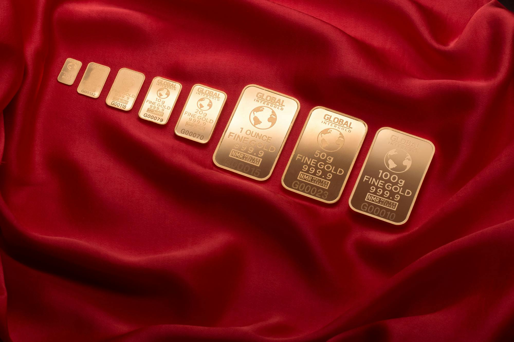 Array of fine gold bars displayed on rich red fabric, symbolizing wealth and luxury.