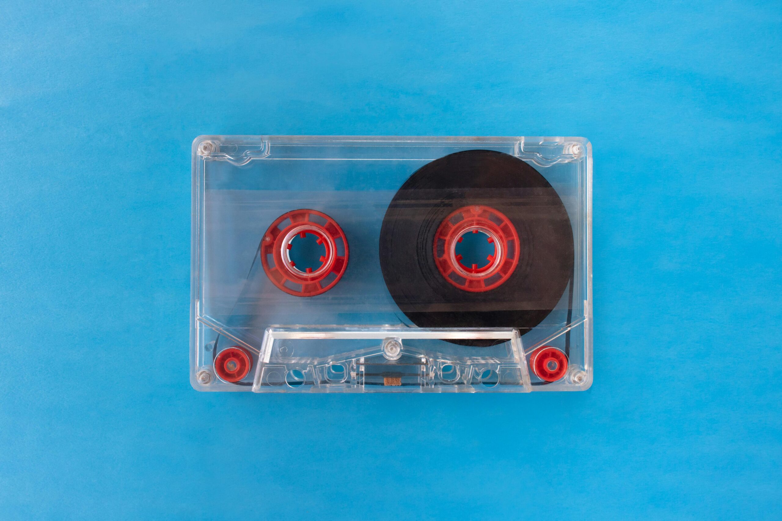 Vintage transparent cassette tape with red reels on a bright blue background.