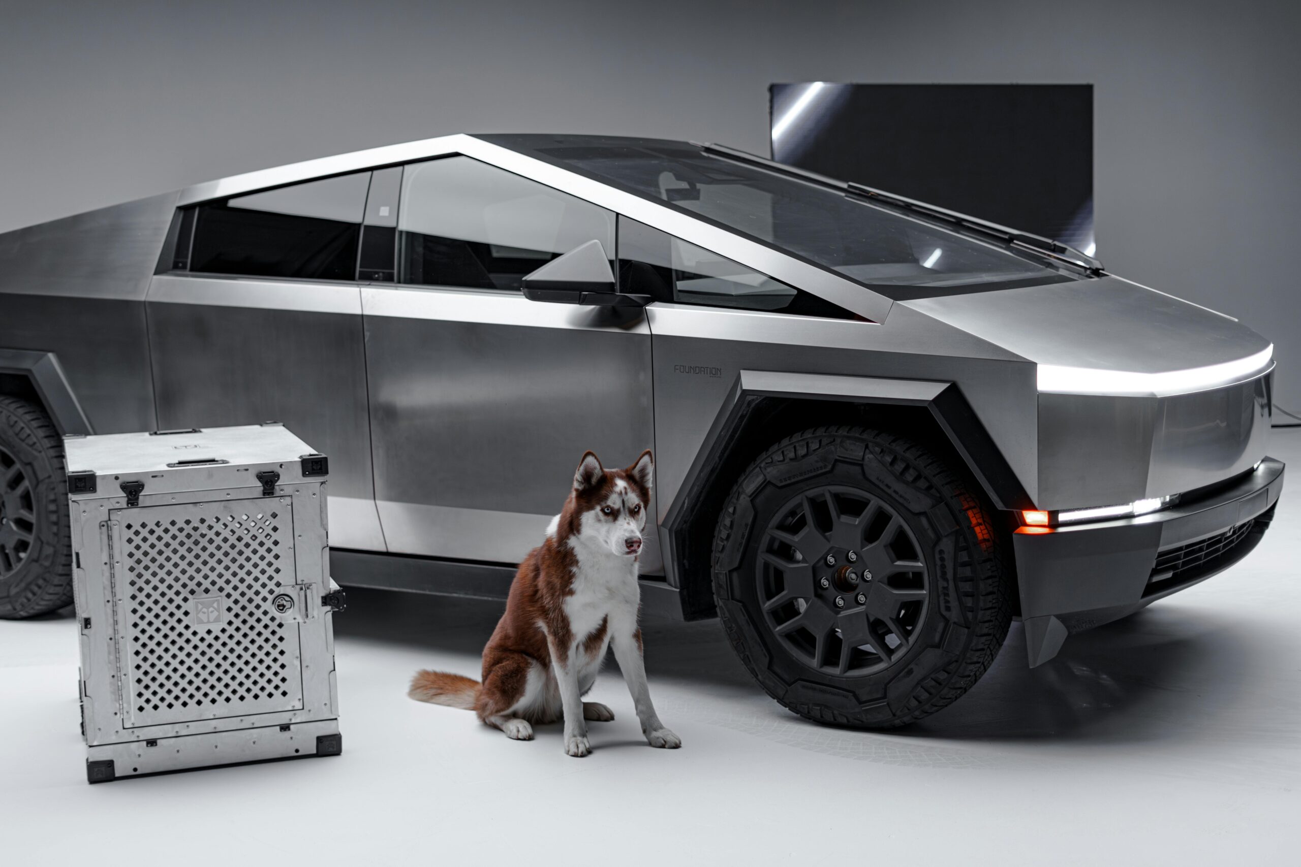 Sleek Cybertruck and Siberian Husky beside a sturdy dog crate, studio setting.