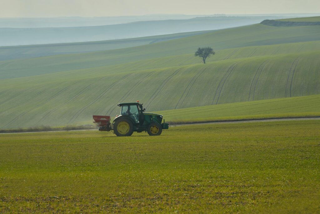 A single tractor traverses rolling green fields under a serene sunset sky.