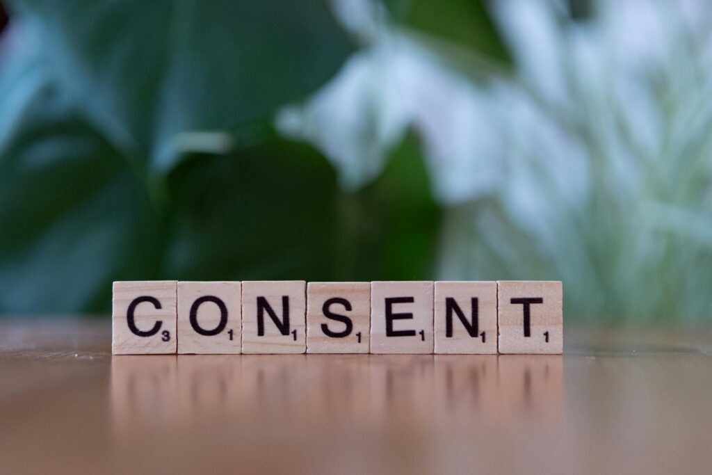 Close-up of Scrabble tiles spelling 'Consent' on a wooden table with a green blurred background.