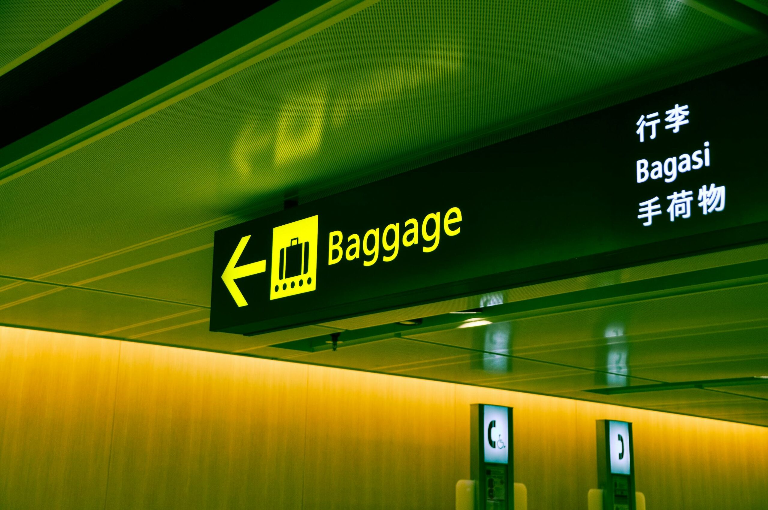 Illuminated airport baggage sign with multilingual translations pointing direction for travelers.