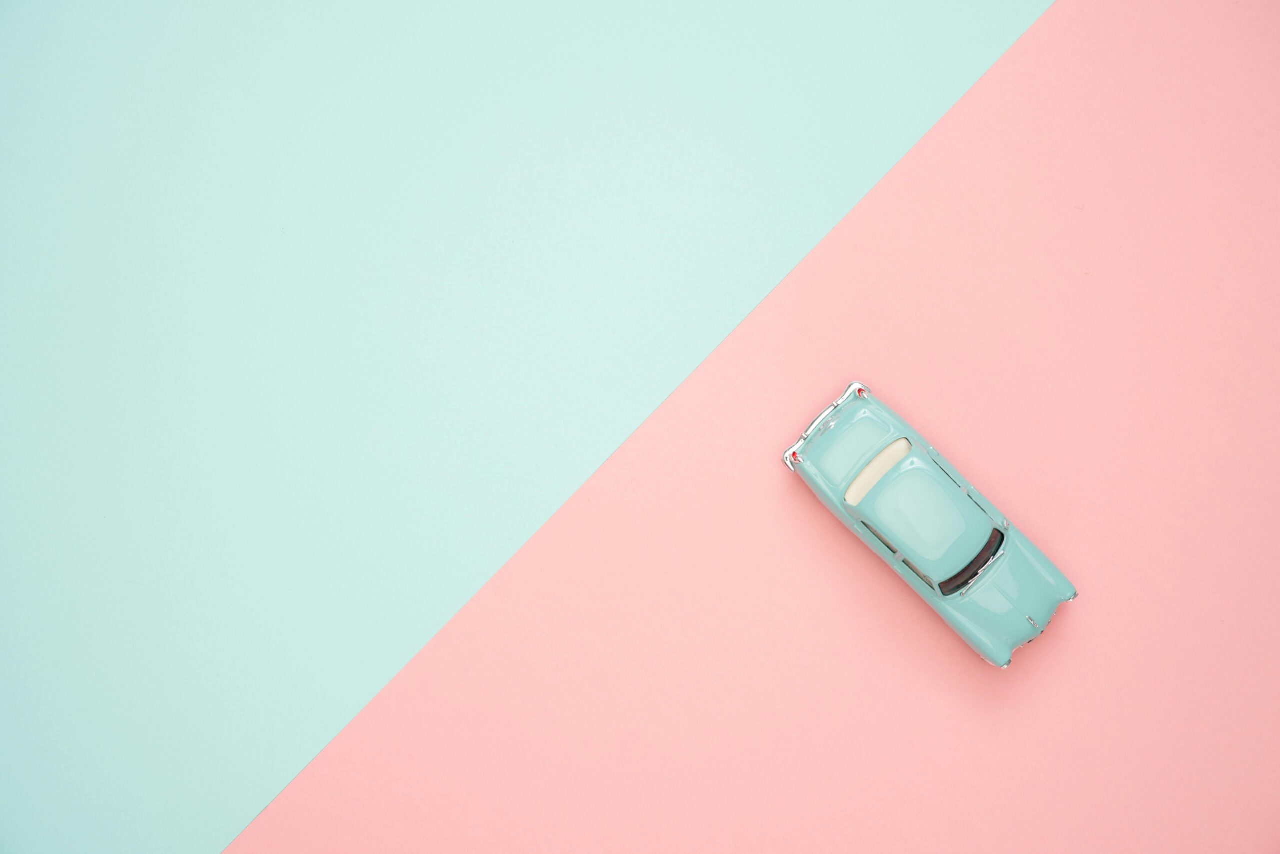 Toy car on a pastel pink and blue background, representing simplicity and retro design.