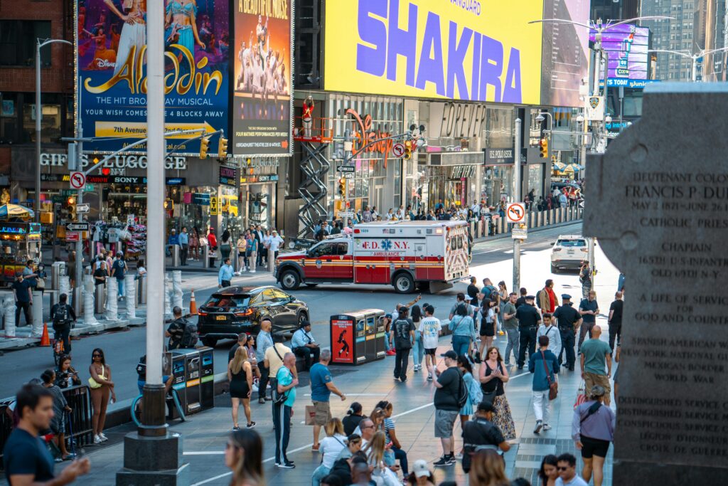 A vibrant view of Times Square, New York City, featuring a busy street with people and an FDNY ambulance.