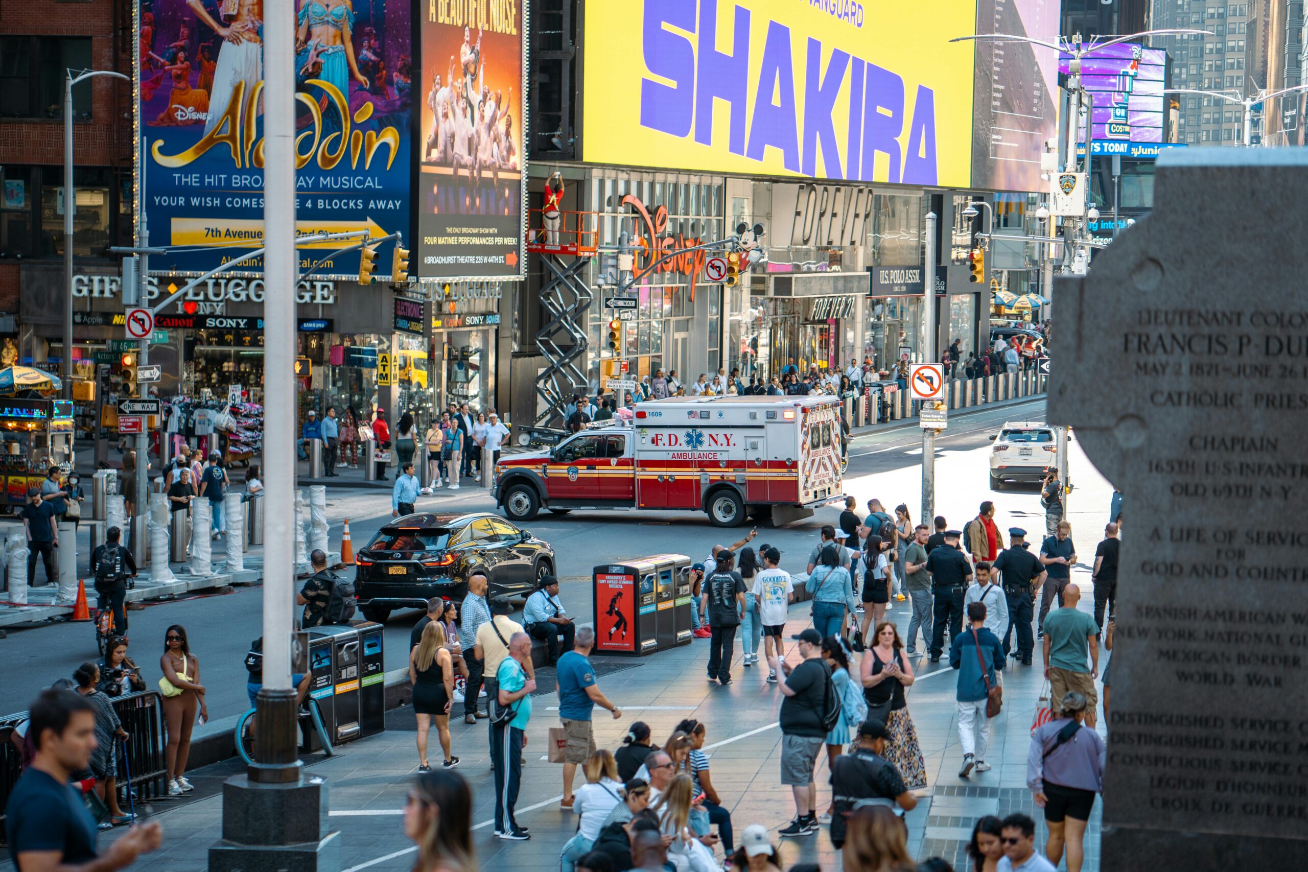 A vibrant view of Times Square, New York City, featuring a busy street with people and an FDNY ambulance.