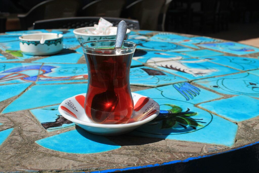 Glass of Turkish tea with spoon on colorful mosaic table in outdoor setting.