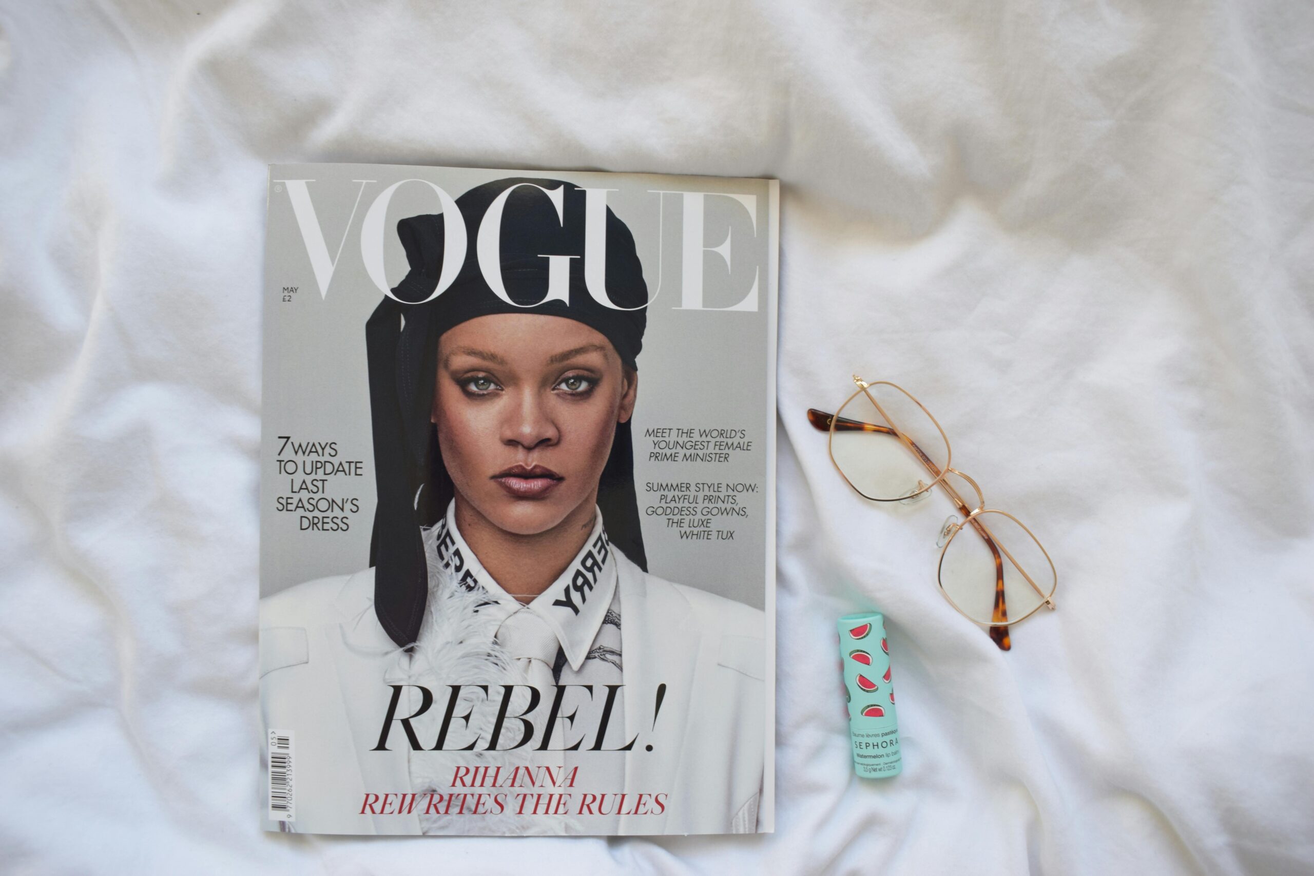 Vogue magazine featuring a celebrity with eyeglasses and lip balm on white fabric.