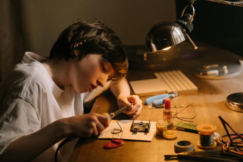 Creative young child engaged in soldering circuit board at home, showcasing technical skills.
