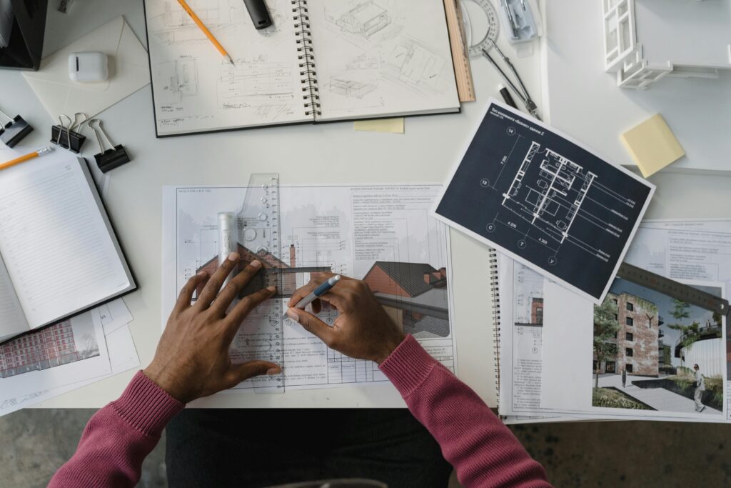 Architect designing plans at a desk surrounded by tools, drafts, and blueprints.