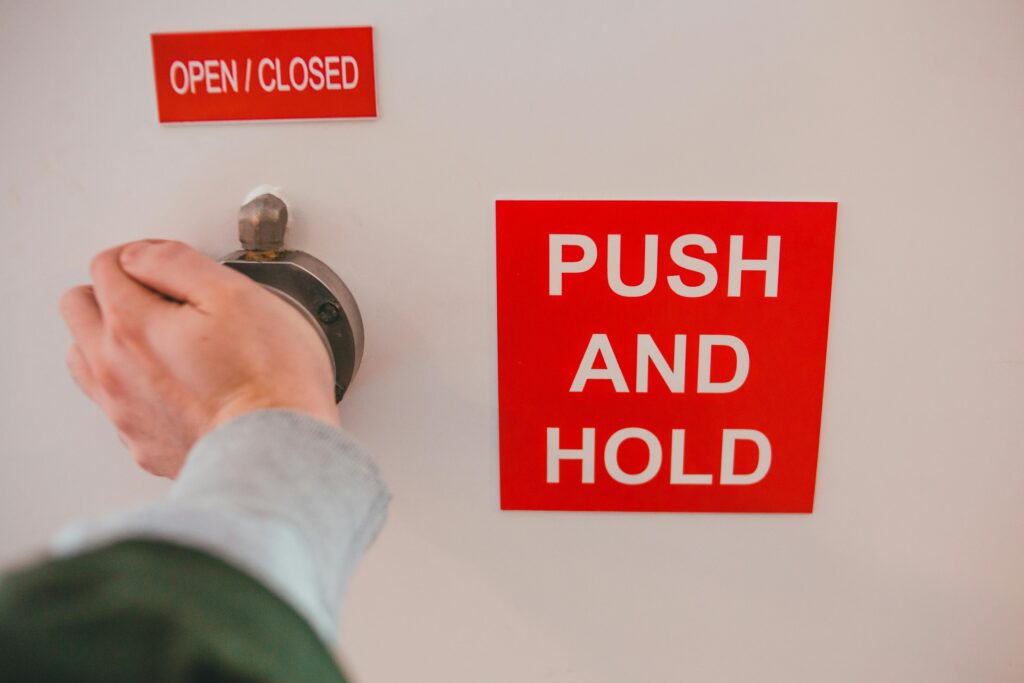Close-up of hand operating knob with red safety signs 'OPEN/CLOSED' and 'PUSH AND HOLD'.