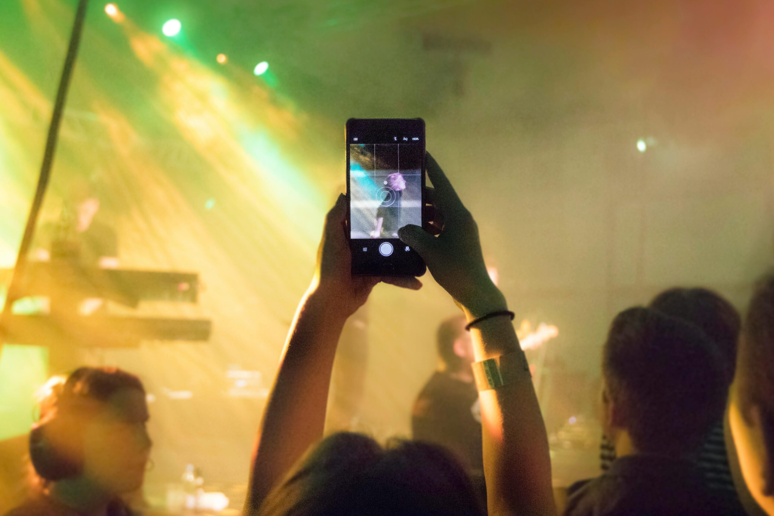 A lively concert crowd captures the performance with vibrant lights and a smartphone focus.