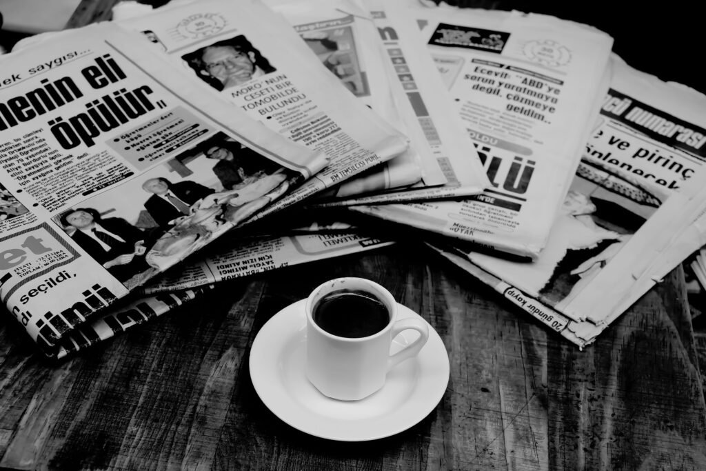 pexels-photo-3953481-3953481 A cup of Turkish coffee sits on a wooden table next to a stack of newspapers.