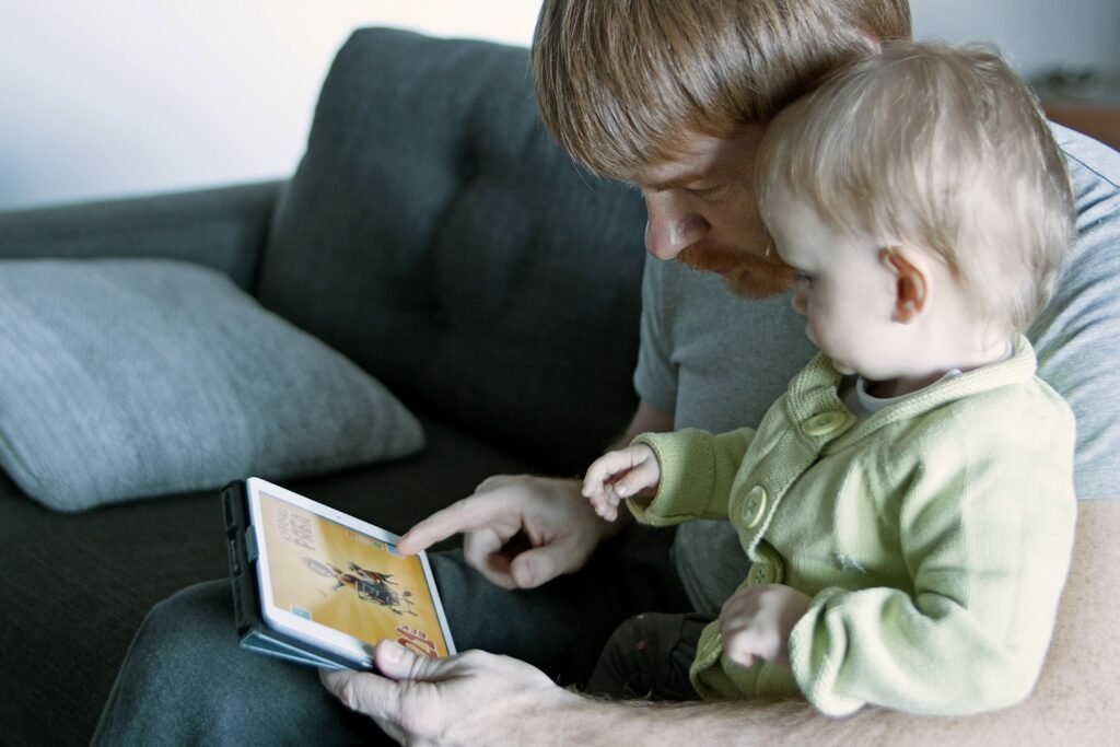 pexels-photo-7414415-7414415 A father and baby sitting on a sofa using a tablet at home.